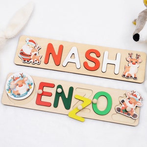 May include: Two wooden puzzle boards with Christmas themes. The top board spells out the name "NASH" with a Santa Claus and reindeer illustration. The bottom board spells out the name "ENZO" with a reindeer illustration.