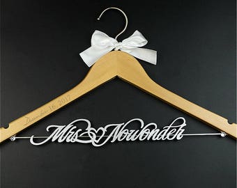 Könnte beinhalten: Ein Holz Kleiderbügel mit einer weißen Satin Schleife und dem Text "December 16, 2017" eingraviert auf der Oberseite. Der Kleiderbügel hat einen silbernen Draht und ein silbernes Glitzer Design, das "Mrs. Nowonder" sagt.