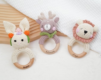 May include: Three crocheted animal teethers with wooden rings. The teethers are a bunny, a deer, and a lion. The rings are engraved with the names "Robin", "Adheem", and "Priya".