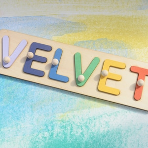 May include: A wooden puzzle with the word "VELVET" spelled out in colorful letters. Each letter has a small white peg in the center.