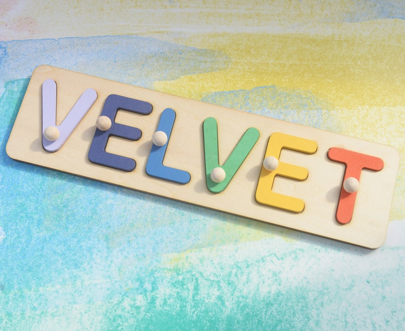 May include: A wooden puzzle with the word "VELVET" spelled out in colorful letters. Each letter has a small white peg in the center.