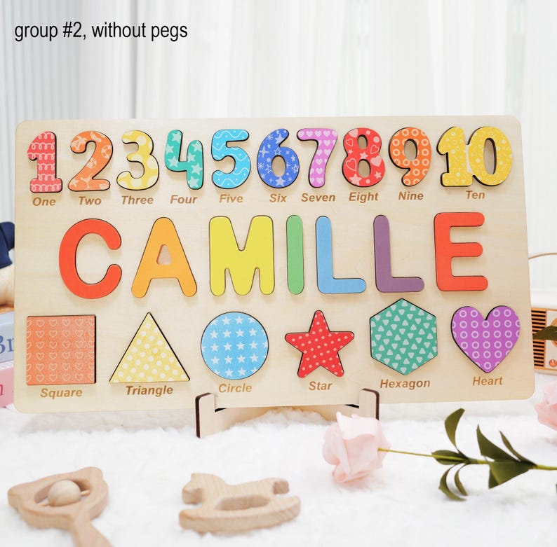 May include: A wooden puzzle with colorful numbers, letters, and shapes. The puzzle features the name "Camille" and the numbers 1 through 10. The shapes include a square, triangle, circle, star, hexagon, and heart.