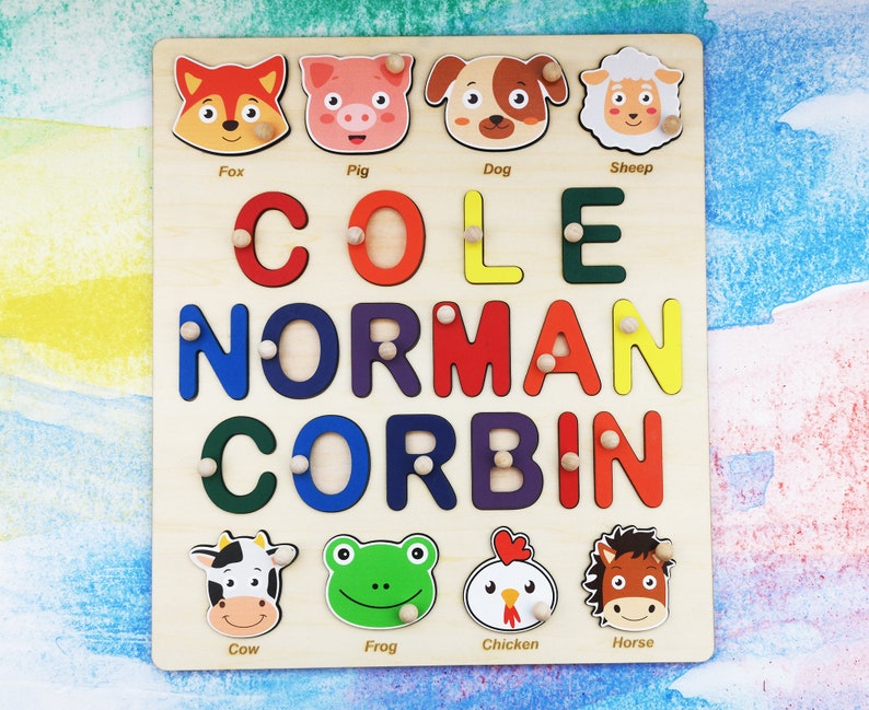 May include: A wooden puzzle with colorful letters spelling out the names "COLE NORMAN CORBIN". The puzzle has animal illustrations with the names "Fox", "Pig", "Dog", "Sheep", "Cow", "Frog", "Chicken", and "Horse" below them.