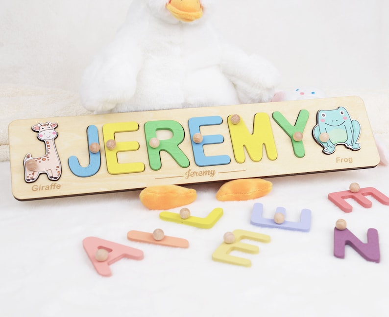 May include: A wooden puzzle with the name "JEREMY" spelled out in colorful letters. The letters are removable and can be placed in the corresponding slots. The puzzle also features a giraffe and a frog.