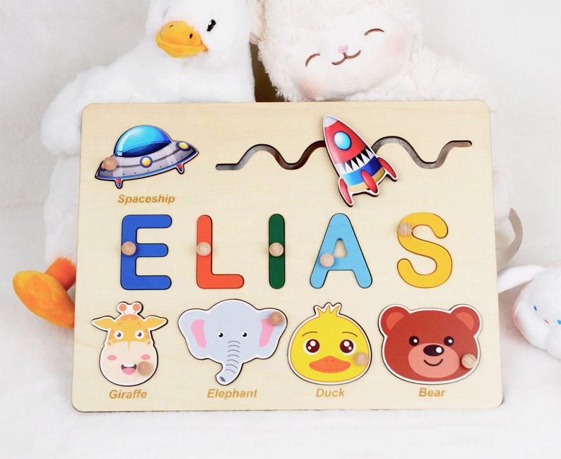 May include: Wooden personalised puzzle with the name ELIAS, featuring a spaceship, rocket, giraffe, elephant, duck, and bear. The puzzle pieces are colourful and have a cartoon style.