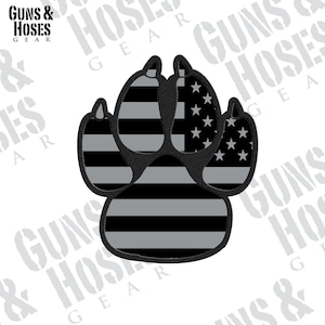 May include: A black and gray paw print with the American flag design. The paw print is a patch or sticker.