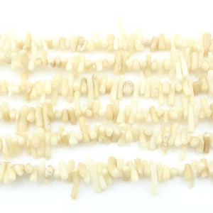 May include: A strand of off-white coral beads. The beads are irregular in shape and size, with some being longer and thinner than others. The beads are strung together on a clear thread.