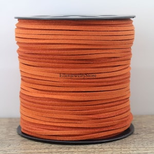 May include: A spool of orange suede cord, perfect for jewelry making or crafting projects. The cord is wound tightly on a black spool.
