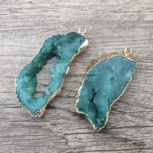 以下が含まれることがあります： 金メッキの縁取りが施された緑色のアゲートクリスタルペンダント2個。クリスタルは自然でざらざらした質感で、上部に吊り下げ用の穴があります。