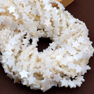 May include: A strand of star-shaped beads in a creamy white hue. The beads are strung together, forming a necklace or strand. The stars have a pearlescent finish, reflecting light. These beads are suitable for jewellery making.