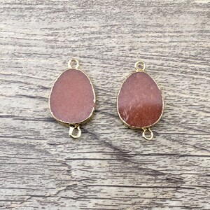May include: Two gold-toned metal connector charms with a reddish-brown stone in the center. The stones are oval shaped and have a slightly textured surface.
