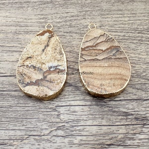 May include: Two brown and white agate stone pendants with gold-toned metal bail loops. The stones have a natural, marbled pattern.