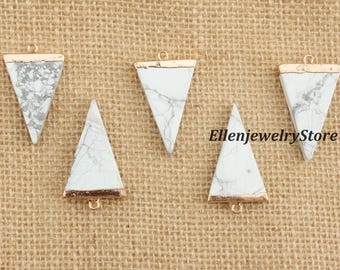 May include: Five white and gray triangle pendants with gold-colored trim and a small loop at the top. The pendants have a marbled appearance and are displayed on a textured, tan surface. The text "EllenjewelryStore" is visible.