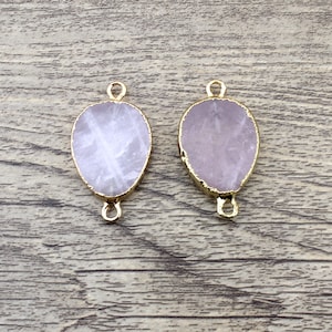 Puede incluir: Dos abalorios conectores ovalados de cuarzo rosa con bucles de metal dorado a cada lado. Los abalorios son de color rosa pálido y tienen un acabado natural en bruto.