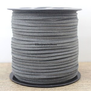 Puede incluir: Un carrete de cordón de ante gris, enrollado alrededor de un carrete de plástico negro. El cordón tiene aproximadamente 3 mm de ancho.