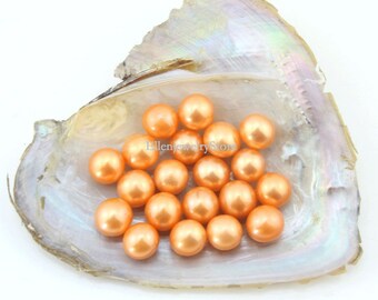 May include: A close-up of a group of 20 peach-colored round pearls in a white seashell. The pearls are smooth and shiny.