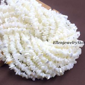 Puede incluir: Primer plano de hileras de cuentas de concha blancas. Las cuentas son pequeñas, de forma irregular y están ensartadas. Las cuentas son de color blanco cremoso y tienen un acabado pulido. El texto "EllenjewelryStore" es visible.