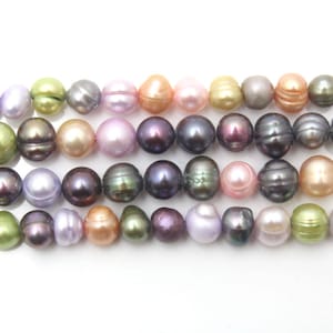 Puede incluir: Una hebra de cuentas de perlas surtidas en varios colores, incluyendo rosa, morado, verde y negro. Las perlas son redondas y tienen un acabado liso y brillante.