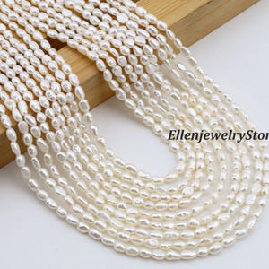 Puede incluir: Primer plano de múltiples hilos de perlas blancas de forma ovalada. Las perlas están ensartadas juntas, creando un efecto en capas. El fondo es una superficie de madera de color claro. El texto "EllenjewelryStore" es visible.