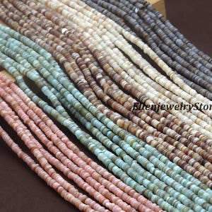 Peut inclure: Gros plan de plusieurs brins de petites perles plates en coquillage de différentes couleurs. Les perles sont disposées en rangées parallèles, présentant une palette de tons roses, bleus, bruns, crème et gris. Les perles sont probablement destinées à la fabrication de bijoux.