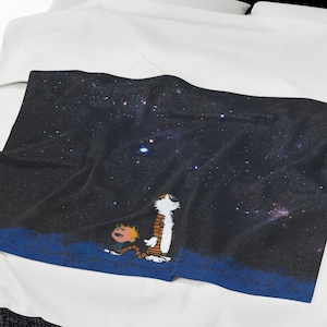 May include: A white bed with a black headboard and a white duvet cover. The duvet cover has a printed image of two cartoon characters looking up at a starry night sky.