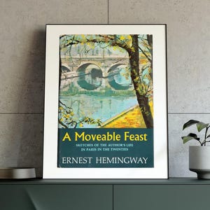 May include: A green cabinet with three doors and gold legs. A framed book cover with a painting of a bridge and the title "A Moveable Feast" by Ernest Hemingway is on top of the cabinet.