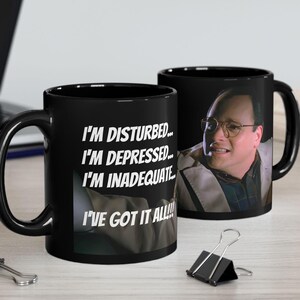 Op de afbeelding: Zwarte keramische koffiemok met een witte afbeelding van een man met een verraste uitdrukking. De mok heeft de tekst "I'm disturbed... I'm depressed... I'm inadequate... I've got it all!"