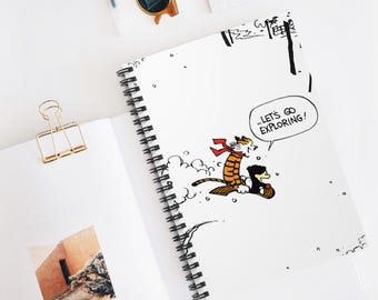 Può includere: Quaderno bianco a spirale con un'illustrazione a fumetti di una tigre e un pinguino che vanno in slitta, con la scritta "...LET'S GO EXPLORING!". Sono visibili anche una graffetta dorata e occhiali da sole.