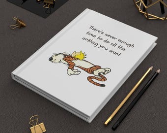 Può includere: Quaderno con copertina rigida bianca con un'illustrazione a cartoni animati di Calvin e Hobbes. La copertina mostra il testo "There's never enough time to do all the nothing you want." Sono visibili anche matite e fermagli dorati e neri.