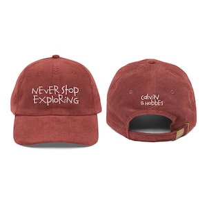 Może przedstawiać: Czapka bejsbolowa z sztruksu w kolorze ceglastym z napisem "NEVER STOP EXPLORING" wyhaftowanym z przodu. Z tyłu czapki znajduje się napis "calvin & hobbes". Czapka ma regulowany pasek.