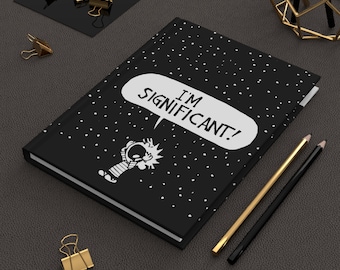 Peut inclure: Journal noir avec des pois blancs et le texte "I'M SIGNIFICANT!" dans une bulle de dialogue. Le journal présente une illustration de personnage de dessin animé. Des crayons dorés et noirs et des trombones dorés sont également visibles.