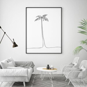 May include: A black and white line drawing of a palm tree in a black frame hanging on a white wall. The frame is above a white couch with gray throw pillows and a white coffee table with a vase and other decorative items.