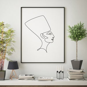 May include: A black and white line drawing of a woman wearing a crown, framed in a black frame and hanging on a white wall. The drawing is in a minimalist style and is a popular choice for modern home decor.