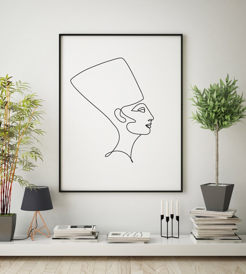 May include: A black and white line drawing of a woman wearing a crown, framed in a black frame and hanging on a white wall. The drawing is in a minimalist style and is a popular choice for modern home decor.