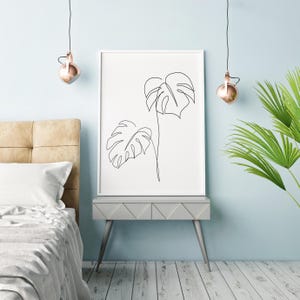 May include: A black and white line drawing of two tropical leaves on a white background. The drawing is framed and hanging on a light blue wall.
