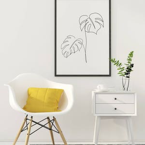 May include: A white chair with a yellow pillow sits on a gray rug in front of a white nightstand with two drawers. A framed black and white line drawing of two tropical leaves hangs on the wall above the nightstand.