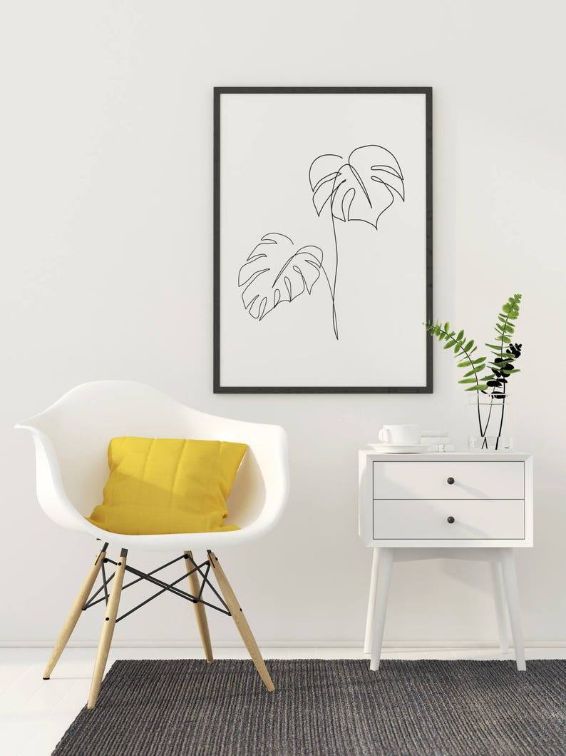 May include: A white chair with a yellow pillow sits on a gray rug in front of a white nightstand with two drawers. A framed black and white line drawing of two tropical leaves hangs on the wall above the nightstand.