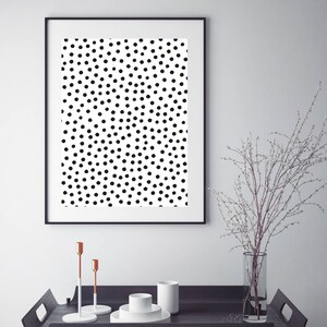 May include: A framed art print featuring a black and white polka dot pattern. The artwork is displayed above a dark wooden tray with decorative items, including candlesticks and a vase with branches.