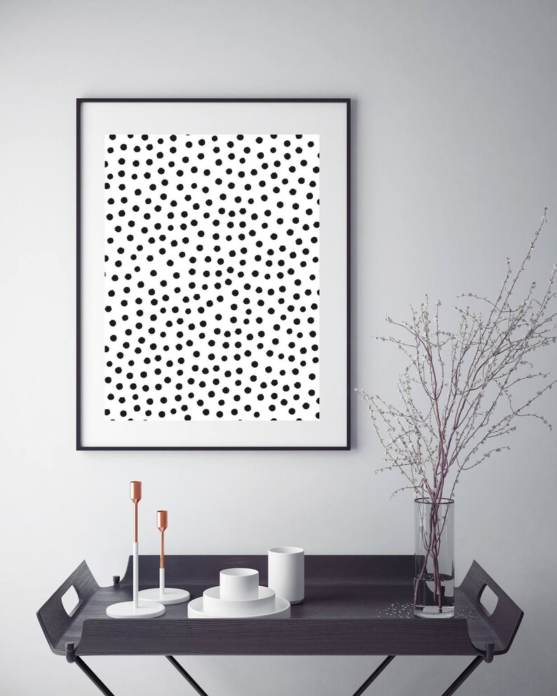 May include: A framed art print featuring a black and white polka dot pattern. The artwork is displayed above a dark wooden tray with decorative items, including candlesticks and a vase with branches.