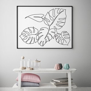 May include: A black and white line drawing of tropical leaves in a black frame hanging on a white wall above a white shelf with two clear glass jars, a wooden knob, and three colorful ceramic candle holders.