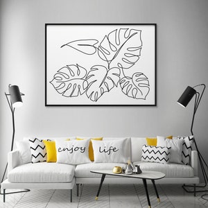 May include: A white couch with yellow and black patterned throw pillows. The pillows have the words "enjoy" and "life" printed on them. A black and white line drawing of tropical leaves is framed and hanging on the wall above the couch.