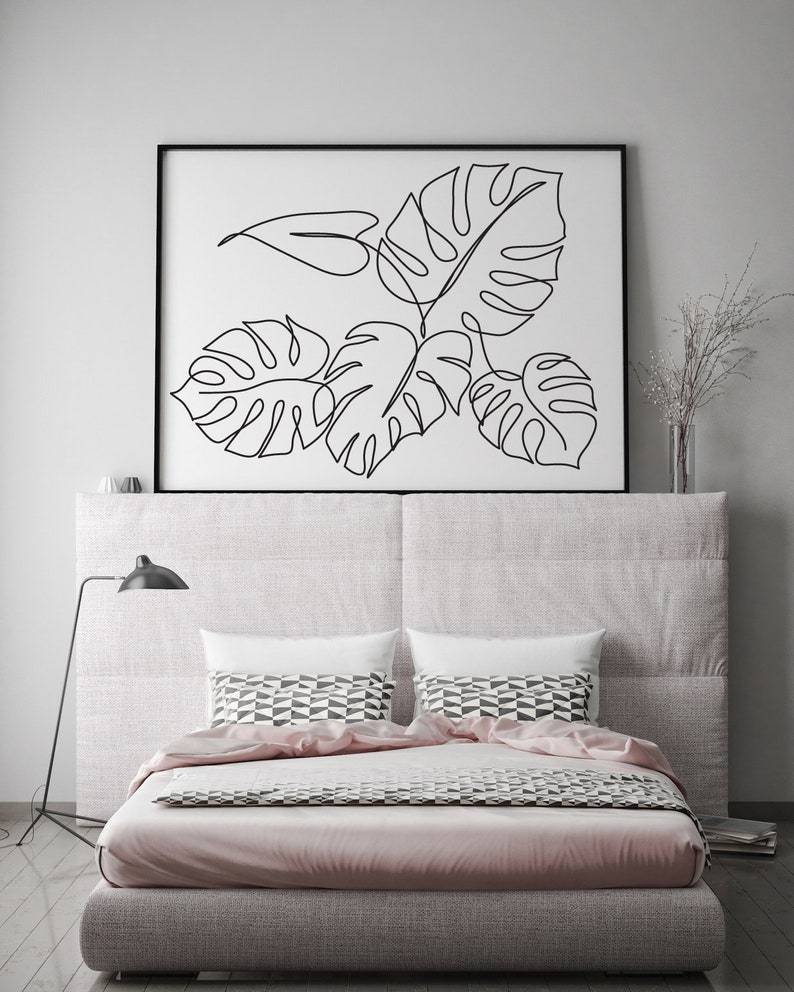 May include: A black and white line drawing of tropical leaves in a black frame above a bed with a pink duvet and patterned pillows.