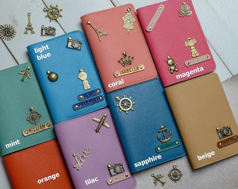 May include: A collection of colorful passport holders in various shades, including light blue, coral, magenta, and beige. Each holder is adorned with decorative metal charms and personalized name tags. The image includes the text "light blue", "coral", "magenta", "beige".