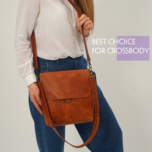 Puede incluir: Un bolso bandolera de cuero marr&oacute;n con solapa y correa ajustable. El bolso se lleva al hombro. El texto "BEST CHOICE FOR CROSSBODY" est&aacute; en un recuadro morado.