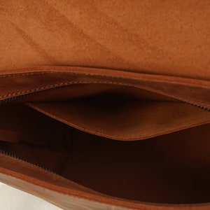 Puede incluir: Vista abierta de un bolso de cuero marr&oacute;n. El bolso presenta un compartimento principal grande y un bolsillo m&aacute;s peque&ntilde;o. Se ven una cremallera y una solapa. El cuero tiene un aspecto natural y texturizado.
