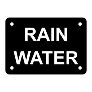 May include: A rectangular black sign with rounded corners and four white dots, one in each corner. The words "RAIN WATER" are printed in large, bold, white letters, centered on the sign.