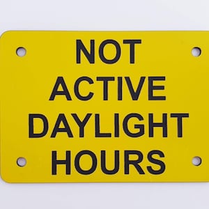 Op de afbeelding: Een geel bord met zwarte tekst dat "NOT ACTIVE DAYLIGHT HOURS" aangeeft. Het bord heeft vier gaten in de hoeken.