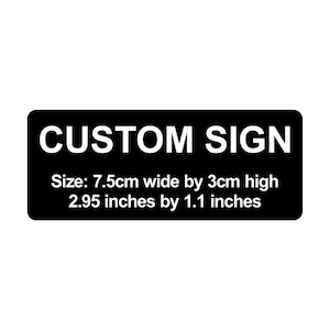 May include: A black rectangular sign with rounded corners. The white text reads "CUSTOM SIGN". Below, the size is listed as 7.5cm wide by 3cm high, or 2.95 inches by 1.1 inches.