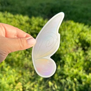 May include: A single iridescent white fairy wing sticker with a delicate design. The sticker is translucent and has a subtle shimmer.