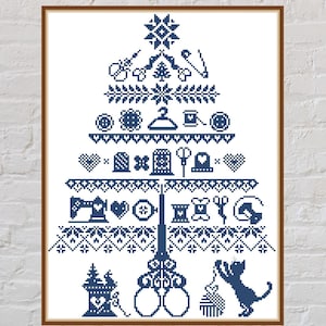 May include: A framed cross-stitch design in navy blue, shaped like a Christmas tree. The tree is composed of sewing-related icons, including scissors, needles, spools of thread, and a cat playing with a spool. The background is a white brick wall.